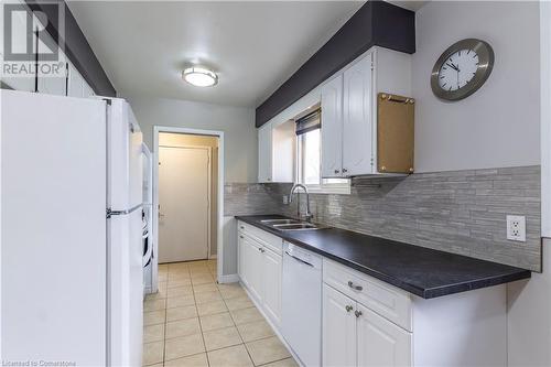 Kitchen featuring backsplash, white appliances, sink, light tile patterned floors, and white cabinetry - 39 Keewatin Avenue, Kitchener, ON - Indoor Photo Showing Kitchen With Double Sink