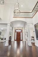 Entrance foyer featuring ornate columns, dark wood-type flooring, and a chandelier - 