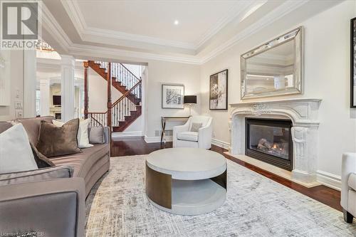 Living room featuring ornate columns, a premium fireplace, wood-type flooring, a tray ceiling, and ornamental molding - 1143 Riverbank Way, Oakville, ON 