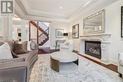 Living room featuring ornate columns, a premium fireplace, wood-type flooring, a tray ceiling, and ornamental molding - 