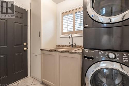 Laundry area featuring cabinets, light tile patterned floors, stacked washer / drying machine, and sink - 146 Kitty Murray Lane, Ancaster, ON - Indoor Photo Showing Laundry Room