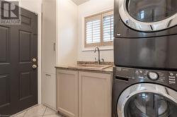 Laundry area featuring cabinets, light tile patterned floors, stacked washer / drying machine, and sink - 