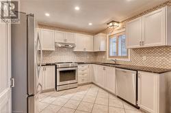 Kitchen with appliances with stainless steel finishes, backsplash, white cabinetry, and sink - 