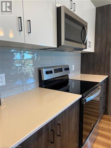 Kitchen featuring white cabinets, decorative backsplash, light wood-type flooring, appliances with stainless steel finishes, and dark brown cabinets - 28 Westhill Drive Unit# 206, Waterloo, ON - Indoor Photo Showing Kitchen