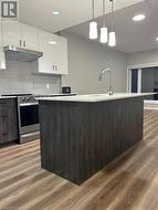 Kitchen featuring decorative light fixtures, light wood-type flooring, and white cabinetry - 