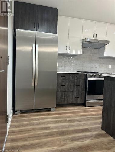 Kitchen featuring white cabinets, light wood-type flooring, stainless steel appliances, and tasteful backsplash - 28 Westhill Drive Unit# 206, Waterloo, ON - Indoor Photo Showing Kitchen With Stainless Steel Kitchen With Upgraded Kitchen