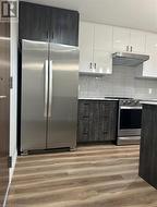 Kitchen featuring white cabinets, light wood-type flooring, stainless steel appliances, and tasteful backsplash - 