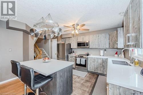 Kitchen with sink, ceiling fan, a textured ceiling, appliances with stainless steel finishes, and a kitchen bar - 727 Zermatt Drive, Waterloo, ON - Indoor Photo Showing Kitchen With Double Sink