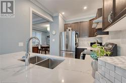 Kitchen with stainless steel fridge, sink, light stone counters, and ornamental molding - 