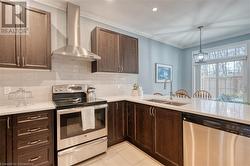 Kitchen with sink, wall chimney exhaust hood, stainless steel appliances, crown molding, and light tile patterned floors - 