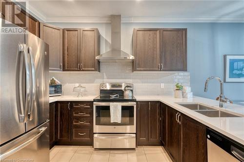 Kitchen featuring wall chimney range hood, crown molding, sink, light tile patterned floors, and appliances with stainless steel finishes - 26 Summerberry Way, Hamilton, ON - Indoor Photo Showing Kitchen With Double Sink With Upgraded Kitchen