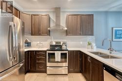 Kitchen featuring wall chimney range hood, crown molding, sink, light tile patterned floors, and appliances with stainless steel finishes - 