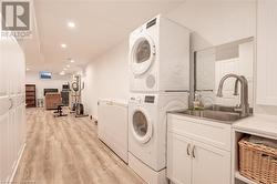 Laundry area with light hardwood / wood-style flooring, cabinets, stacked washer and clothes dryer, and sink - 