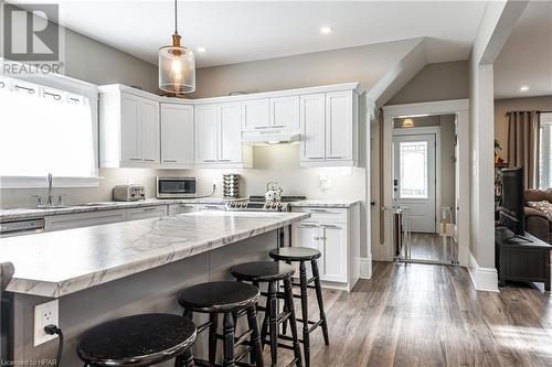 Kitchen with dark wood-type flooring, white cabinets, sink, hanging light fixtures, and a kitchen bar - 175 Mcnab St, Stratford, ON - Indoor Photo Showing Kitchen With Upgraded Kitchen