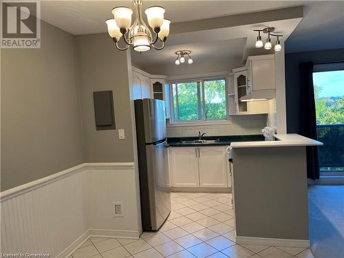 Kitchen with pendant lighting, white cabinets, light tile patterned floors, stainless steel refrigerator, and a chandelier - 2373 King Street E Unit# 48, Hamilton, ON - Indoor Photo Showing Kitchen With Double Sink