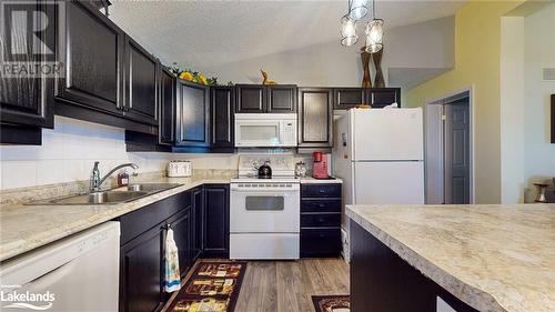 Kitchen with white appliances, dark wood-type flooring, sink, vaulted ceiling, and decorative light fixtures - 69 St James Place, Wasaga Beach, ON - Indoor Photo Showing Kitchen With Double Sink