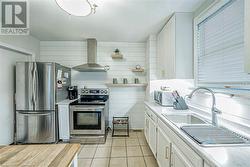 Kitchen with white cabinetry, sink, wall chimney exhaust hood, stainless steel appliances, and light tile patterned floors - 