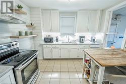 Kitchen featuring wood counters, sink, light tile patterned floors, white cabinetry, and stainless steel appliances - 