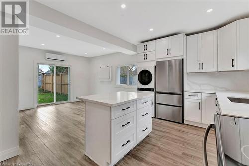 Kitchen in the ADU featuring stainless steel fridge, white cabinetry, a wealth of natural light, and stacked washer and clothes dryer - 306 Paling Avenue, Hamilton, ON - Indoor Photo Showing Kitchen