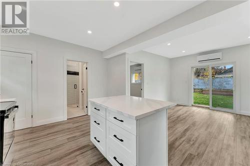 Kitchen in the ADU with range with electric cooktop, white cabinets, a wall mounted AC, a kitchen island, and light wood-type flooring - 306 Paling Avenue, Hamilton, ON - Indoor