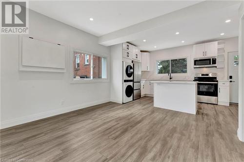 Living Room in the ADU featuring a center island, white cabinets, stacked washing maching and dryer, and appliances with stainless steel finishes - 306 Paling Avenue, Hamilton, ON - Indoor Photo Showing Kitchen