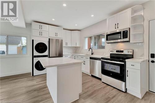 Kitchen in the ADU with stacked washer / drying machine, a kitchen island, white cabinetry, and appliances with stainless steel finishes - 306 Paling Avenue, Hamilton, ON - Indoor Photo Showing Kitchen