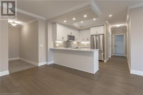 Kitchen with white cabinetry, dark hardwood / wood-style flooring, ornamental molding, and appliances with stainless steel finishes - 460 Callaway Road Unit# 910, London, ON - Indoor Photo Showing Kitchen