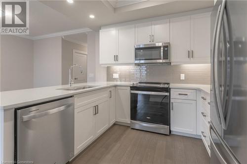 Kitchen featuring hardwood / wood-style floors, white cabinets, ornamental molding, appliances with stainless steel finishes, and kitchen peninsula - 460 Callaway Road Unit# 910, London, ON - Indoor Photo Showing Kitchen With Upgraded Kitchen