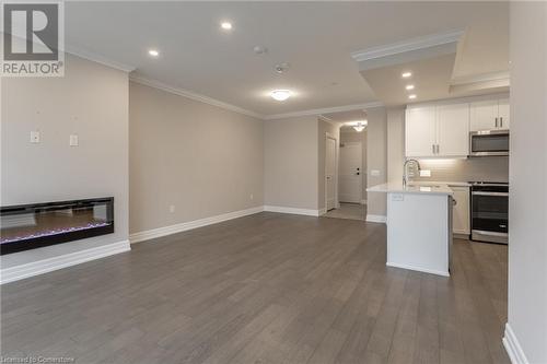 Kitchen featuring white cabinetry, crown molding, hardwood / wood-style floors, decorative backsplash, and appliances with stainless steel finishes - 460 Callaway Road Unit# 910, London, ON - Indoor Photo Showing Kitchen With Fireplace