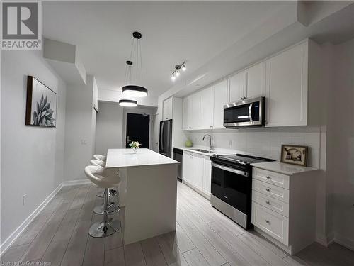 Kitchen with pendant lighting, white cabinets, sink, a kitchen island, and stainless steel appliances - 55 Duke Street W Unit# 1607, Kitchener, ON - Indoor Photo Showing Kitchen