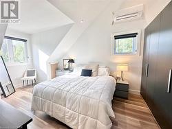 Bedroom featuring lofted ceiling, a wall unit AC, and light hardwood / wood-style flooring - 