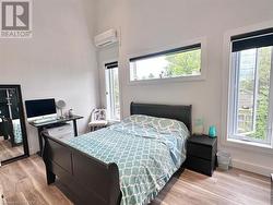 Bedroom featuring light wood-type flooring, an AC wall unit, and multiple windows - 