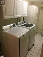 Laundry area featuring cabinets, separate washer and dryer, and light ceramic flooring - 