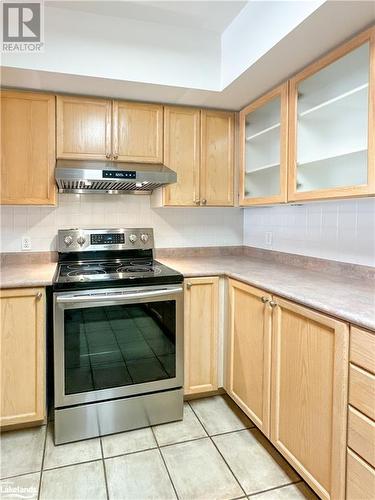 Kitchen with tasteful backsplash, ventilation hood, light brown cabinets, light ceramic tile floors, and stainless steel electric range oven - 16 Raglan Street E Unit# 211, Collingwood, ON - Indoor Photo Showing Kitchen