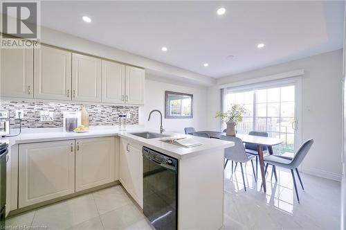 Kitchen with sink, decorative backsplash, light tile patterned floors, black dishwasher, and kitchen peninsula - 1145 Riddell Crescent, Hamilton, ON - Indoor Photo Showing Kitchen