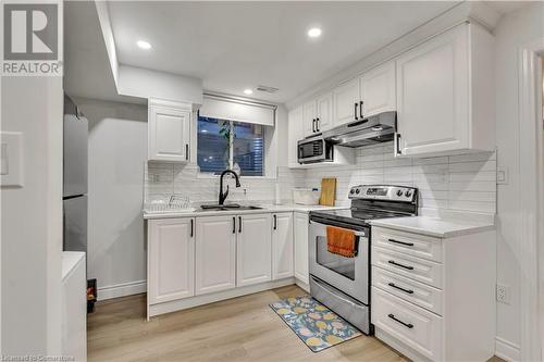 Kitchen featuring white cabinets, light wood-type flooring, appliances with stainless steel finishes, and tasteful backsplash - 48 Isaiah Drive, Kitchener, ON 