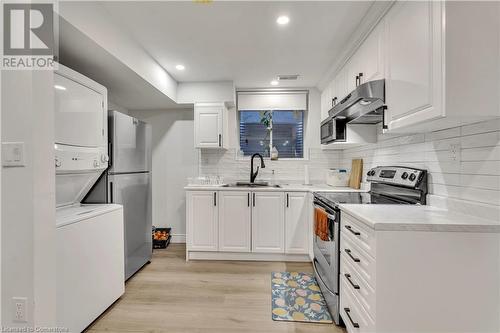 Kitchen with white cabinets, sink, light hardwood / wood-style flooring, stacked washer / dryer, and stainless steel appliances - 48 Isaiah Drive, Kitchener, ON 