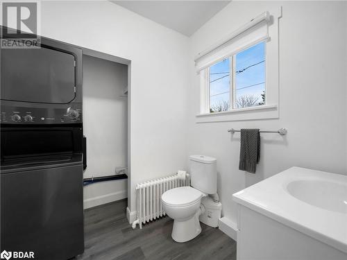 Bathroom featuring radiator, stacked washer / drying machine, toilet, vanity, and hardwood / wood-style flooring - 206 Mary Street, Orillia, ON 