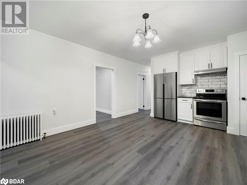 Kitchen with white cabinets, dark hardwood / wood-style floors, appliances with stainless steel finishes, tasteful backsplash, and radiator heating unit - 206 Mary Street, Orillia, ON 