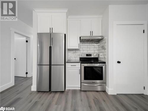 Kitchen with decorative backsplash, appliances with stainless steel finishes, light wood-type flooring, and white cabinetry - 206 Mary Street, Orillia, ON 