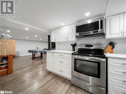 Kitchen with white cabinetry, radiator heating unit, light wood-type flooring, and appliances with stainless steel finishes - 206 Mary Street, Orillia, ON 