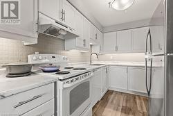 Kitchen with white range with electric stovetop, stainless steel refrigerator, white cabinetry, and sink - 