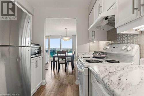 Kitchen featuring decorative backsplash, appliances with stainless steel finishes, light wood-type flooring, white cabinets, and hanging light fixtures - 9 Bonheur Court Unit# 802, Brantford, ON 