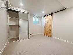 Unfurnished bedroom featuring light carpet, a barn door, and a closet - 