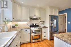 Kitchen featuring appliances with stainless steel finishes, light wood-type flooring, backsplash, sink, and white cabinets - 