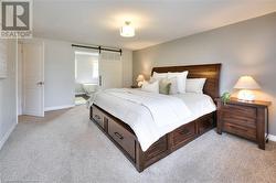 Bedroom with a barn door, ensuite bathroom, and light colored carpet - 