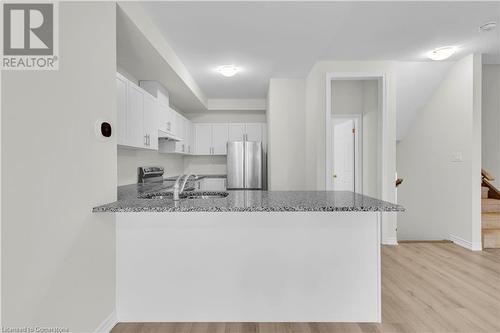 Kitchen with white cabinets, light hardwood / wood-style floors, kitchen peninsula, and stainless steel appliances - 677 Park Road N Unit# 147, Brantford, ON 