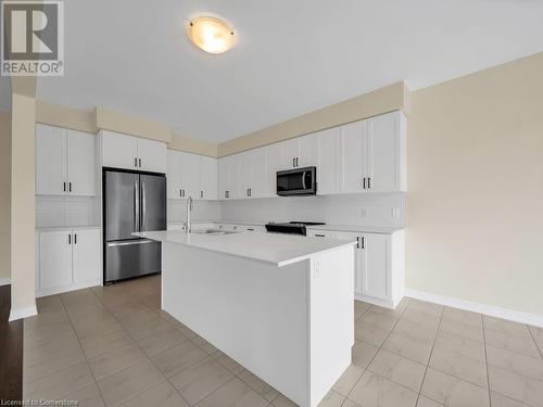 Kitchen with tasteful backsplash, white cabinetry, an island with sink, and stainless steel appliances - 126 Broadacre Drive, Kitchener, ON 