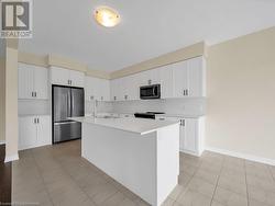 Kitchen with tasteful backsplash, white cabinetry, an island with sink, and stainless steel appliances - 