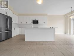 Kitchen featuring stainless steel appliances, white cabinetry, hanging light fixtures, and an island with sink - 